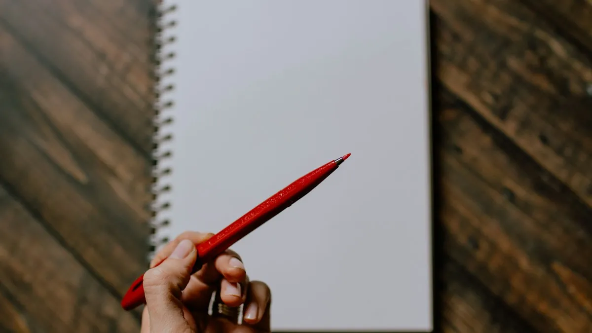 A hand holding a red pencil over a blank notebook page