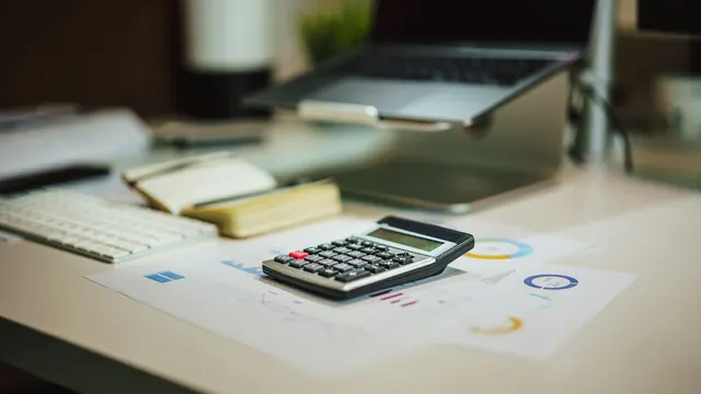 A calculator on a desk next to printed charts and a laptop