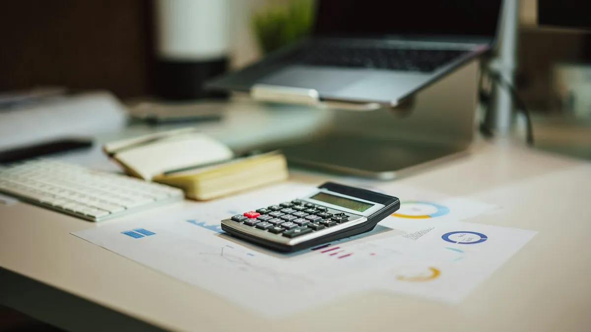 A calculator on a desk next to printed charts and a laptop